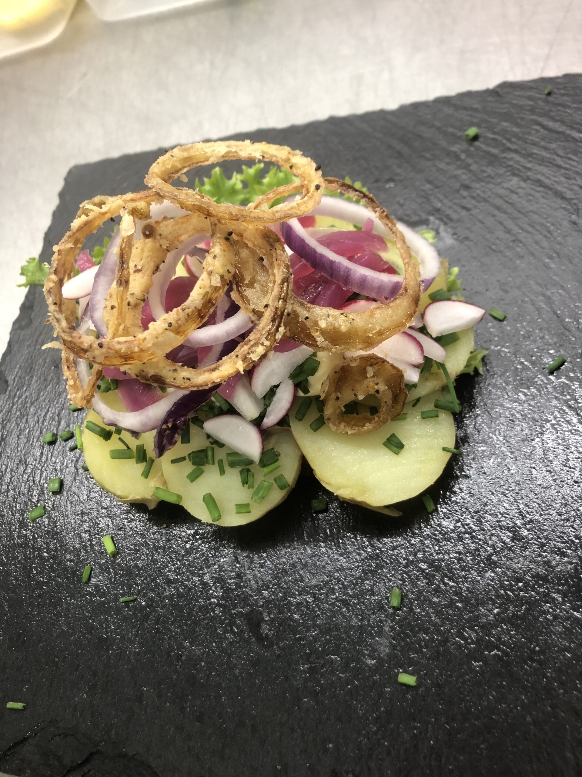 Smørrebrød med kartofler, løgringe og purløg på skiferplade